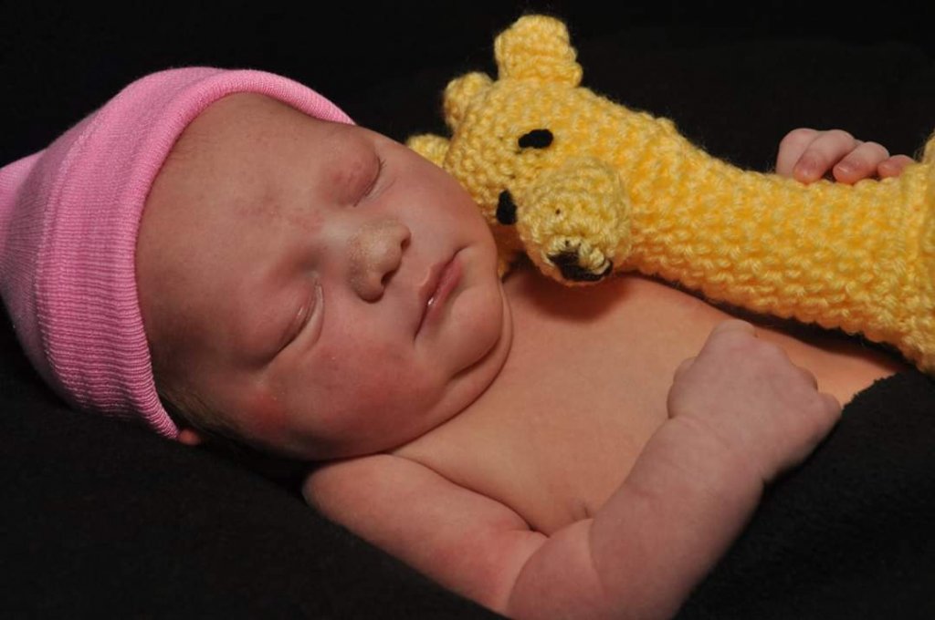 baby girl holding a yellow crocheted baby giraffe with sewn on features to avoid choking hazards