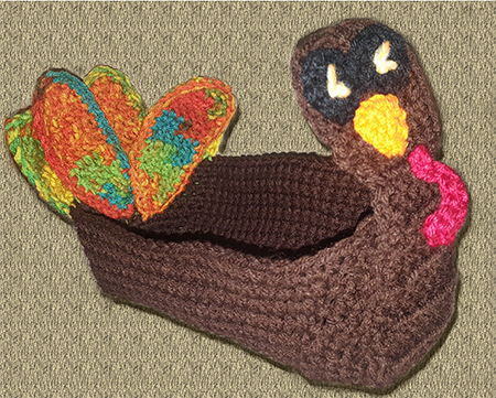crocheted turkey basket adorned with tail feathers and a turkey face. It is made to fit a 10 inch by 5 inch loaf pan.